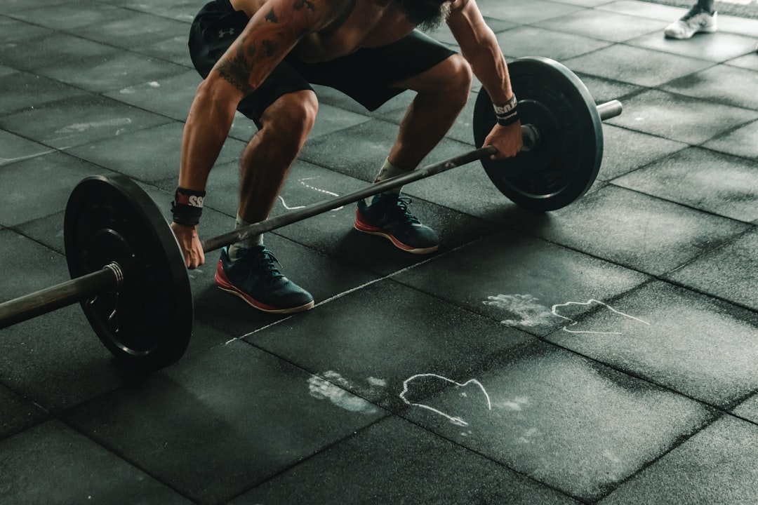 A person lifting a heavy barbell from a black rubber gym floor